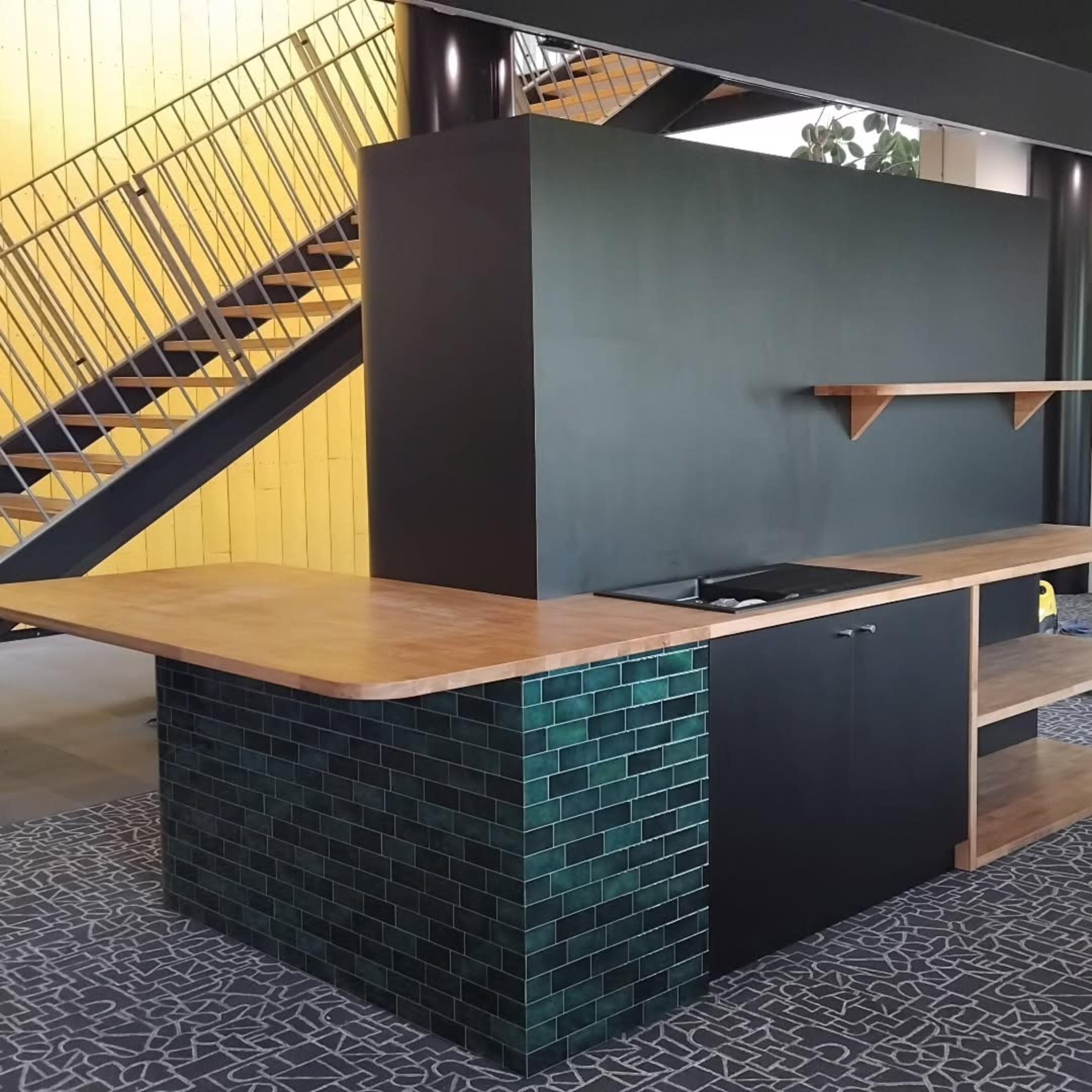 Cuisine en finition bois et carrelage vert bouteille, installée au cœur de l’espace de coworking