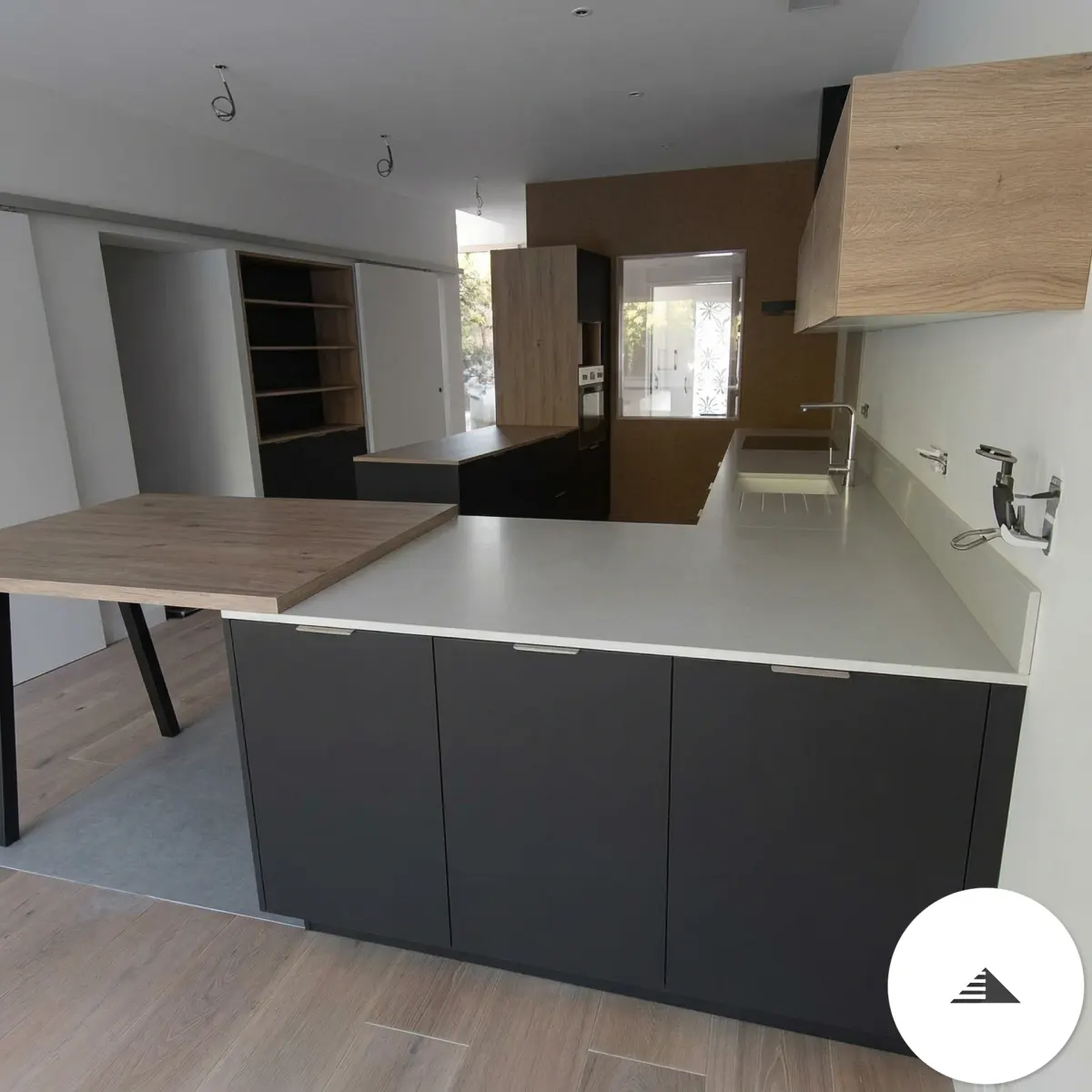 Cuisines sur mesure — Cuisine terminée avec îlot plan blanc, façades anthracite mat et table appoint bois clair sur pied métal, vue espace ouvert à Bastia | Gonzalez Agencement