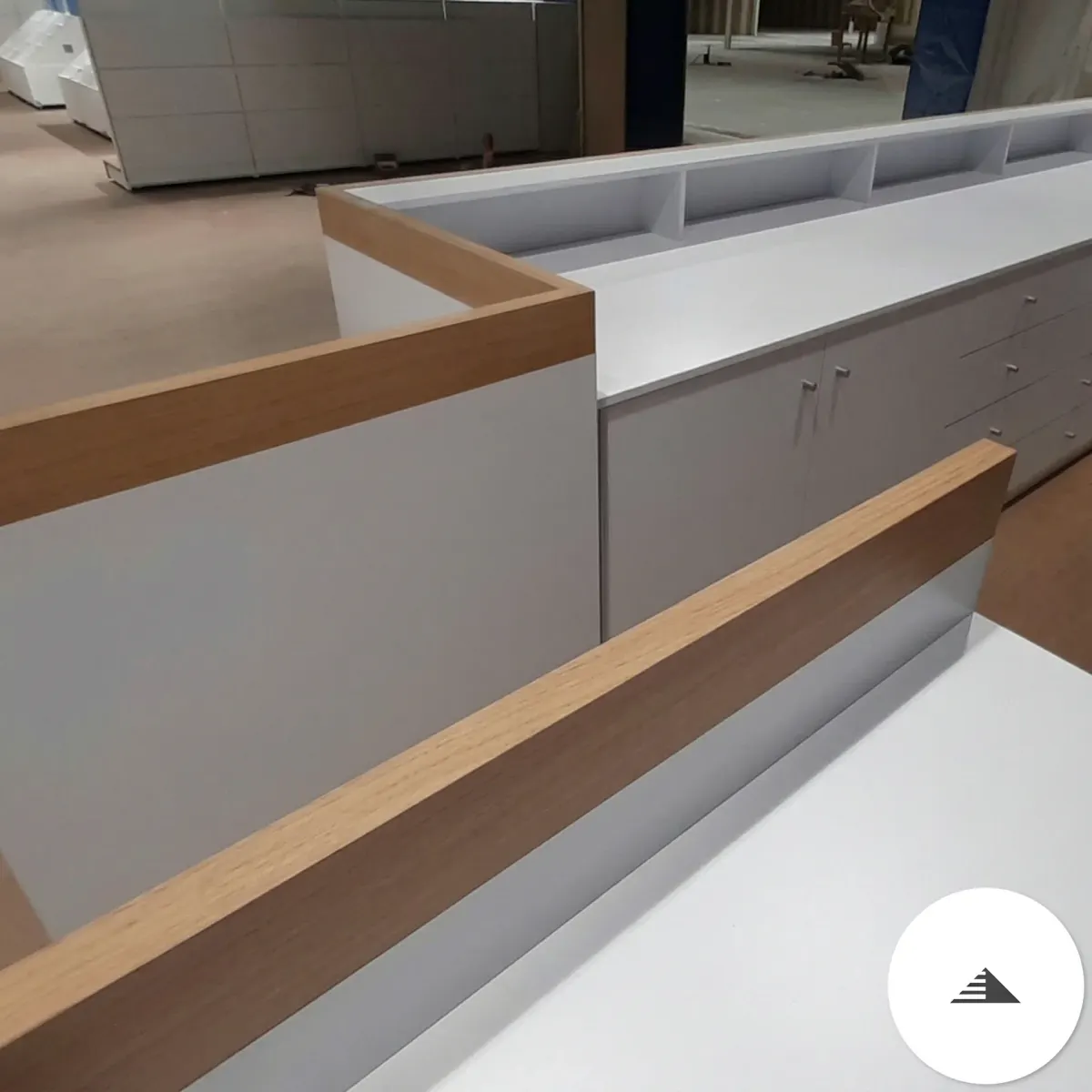 Meubles sur mesure — Banque d'accueil en L laquée gris clair avec bordure chêne naturel, tiroirs et portes, vue d'angle en atelier à Le Pian Médoc | Gonzalez Agencement