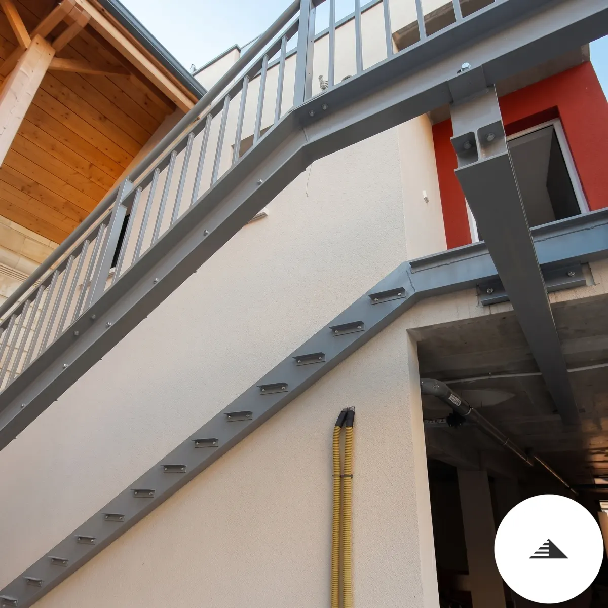 Escaliers sur mesure — Vue de côté de la structure acier courbe sans marches, liselets porteurs apparents, façades bois et rouge en fond à Bordeaux | Gonzalez Agencement