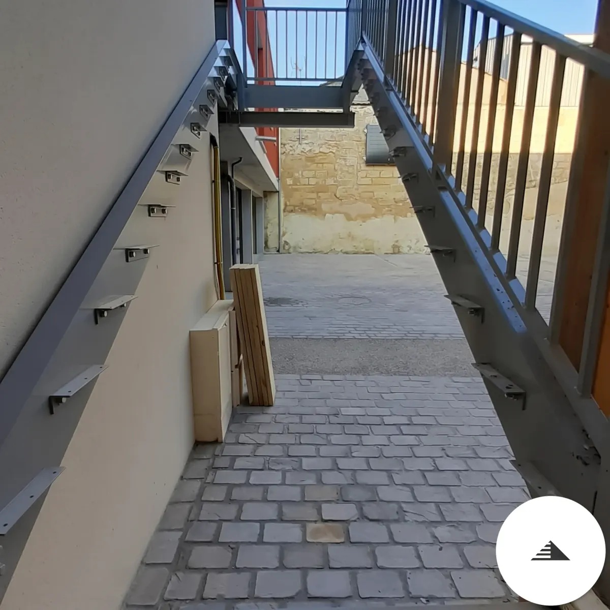 Escaliers sur mesure — Vue de la passerelle pavée au pied de l'escalier, limons acier des deux côtés, chantier en cours à Bordeaux | Gonzalez Agencement