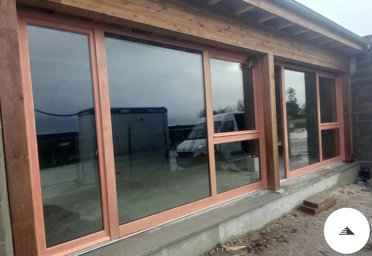 Menuiseries sur mesure — Façade extérieure avec baie vitrée 5 châssis bois massif teinte naturelle, vitrage sombre et structure bois en débord de toit à Bordeaux | Gonzalez Agencement