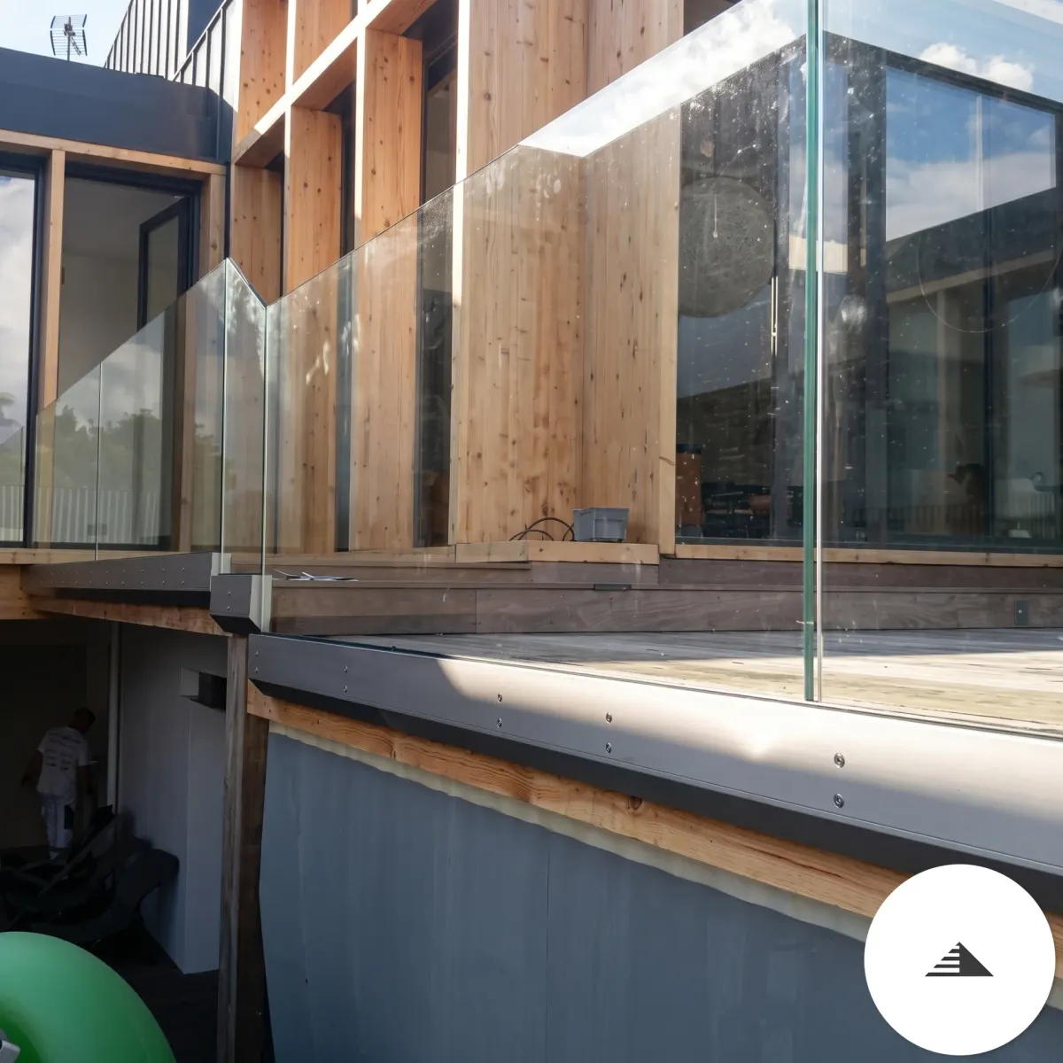 Terrasses sur mesure — Terrasse bois foncé avec garde-corps en panneaux de verre transparent sur sabots noirs, vue en contre-plongée depuis le jardin à Bordeaux | Gonzalez Agencement