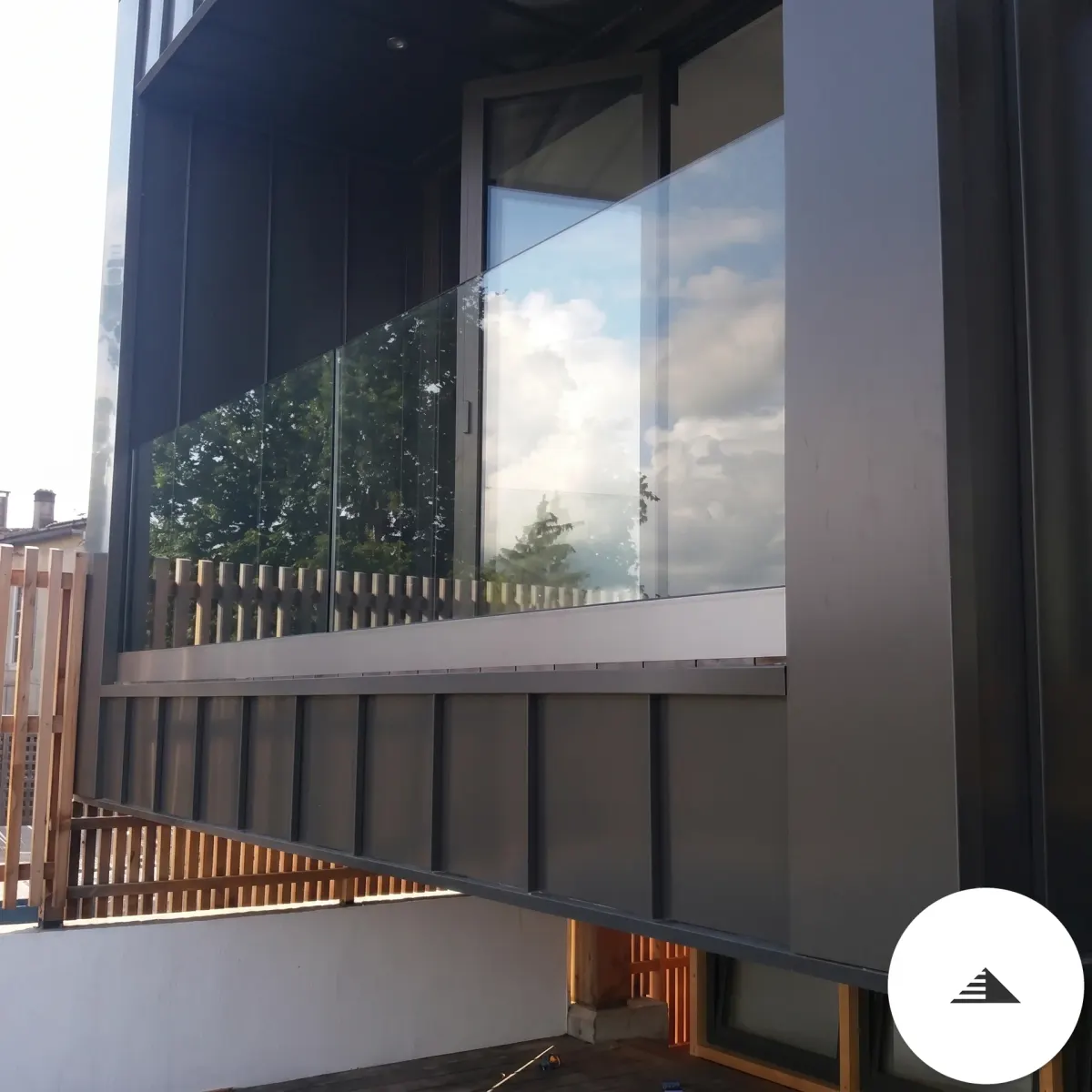 Terrasses sur mesure — Vue frontale d'un balcon avec garde-corps plein verre sur façade noire anthracite, reflets du ciel et des arbres dans le verre à Bordeaux | Gonzalez Agencement