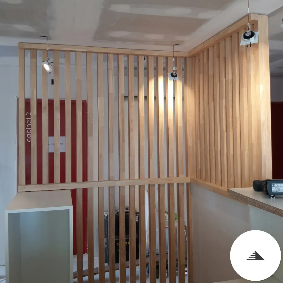 Agencement sur mesure — Vue d'angle du claustra en L formant un coin d'espace, tasseaux bois mis en valeur par des spots de chantier à Bordeaux | Gonzalez Agencement