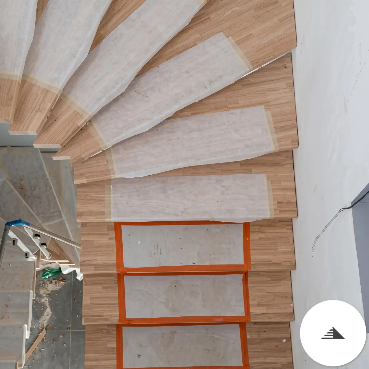 Escaliers sur mesure — Vue de dessous de l'escalier tournant, marches en éventail depuis le limon central, film de protection orange visible à Bordeaux | Gonzalez Agencement