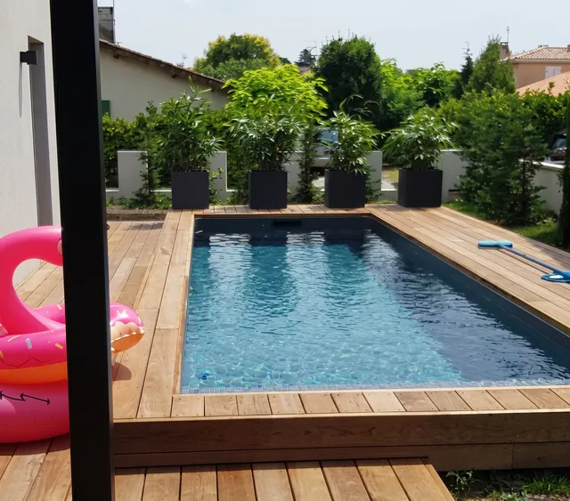Aménagements sur mesure : Terrasse en lames bois naturel clair ceinturant une piscine rectangulaire, vue en plongée légère depuis la pergola à Bordeaux | Gonzalez Agencement