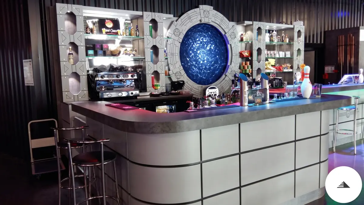 Agencement sur mesure — Comptoir de bar galbé laqué blanc, plan zinc et panneau Stargate circulaire rétroéclairé bleu avec étagères à alcools éclairées à Bordeaux | Gonzalez Agencement